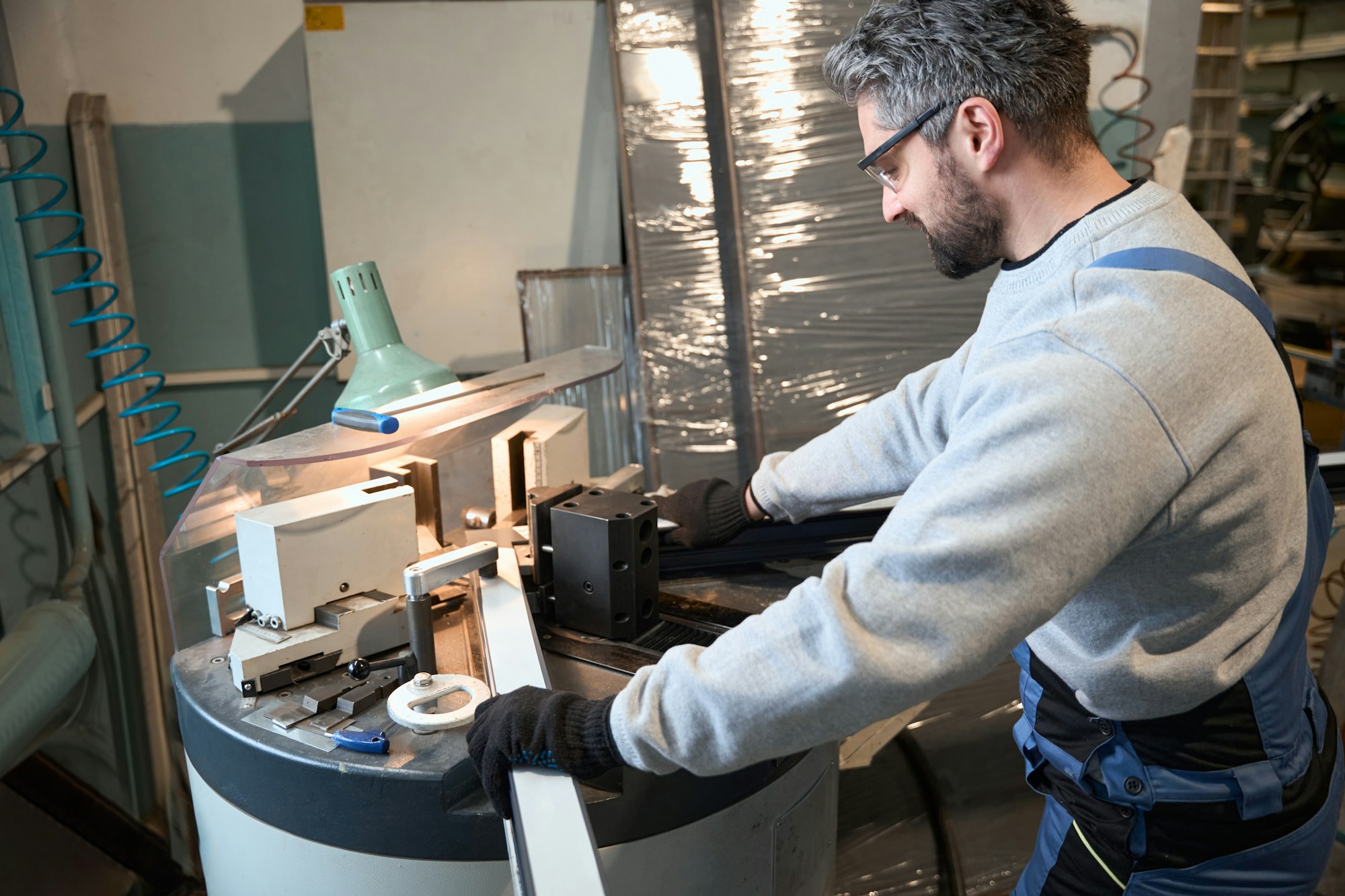 Man in work overalls works on special machine with aluminum profile